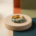 Teal enamel dome band with gold-toned clover studs, adjustable ring